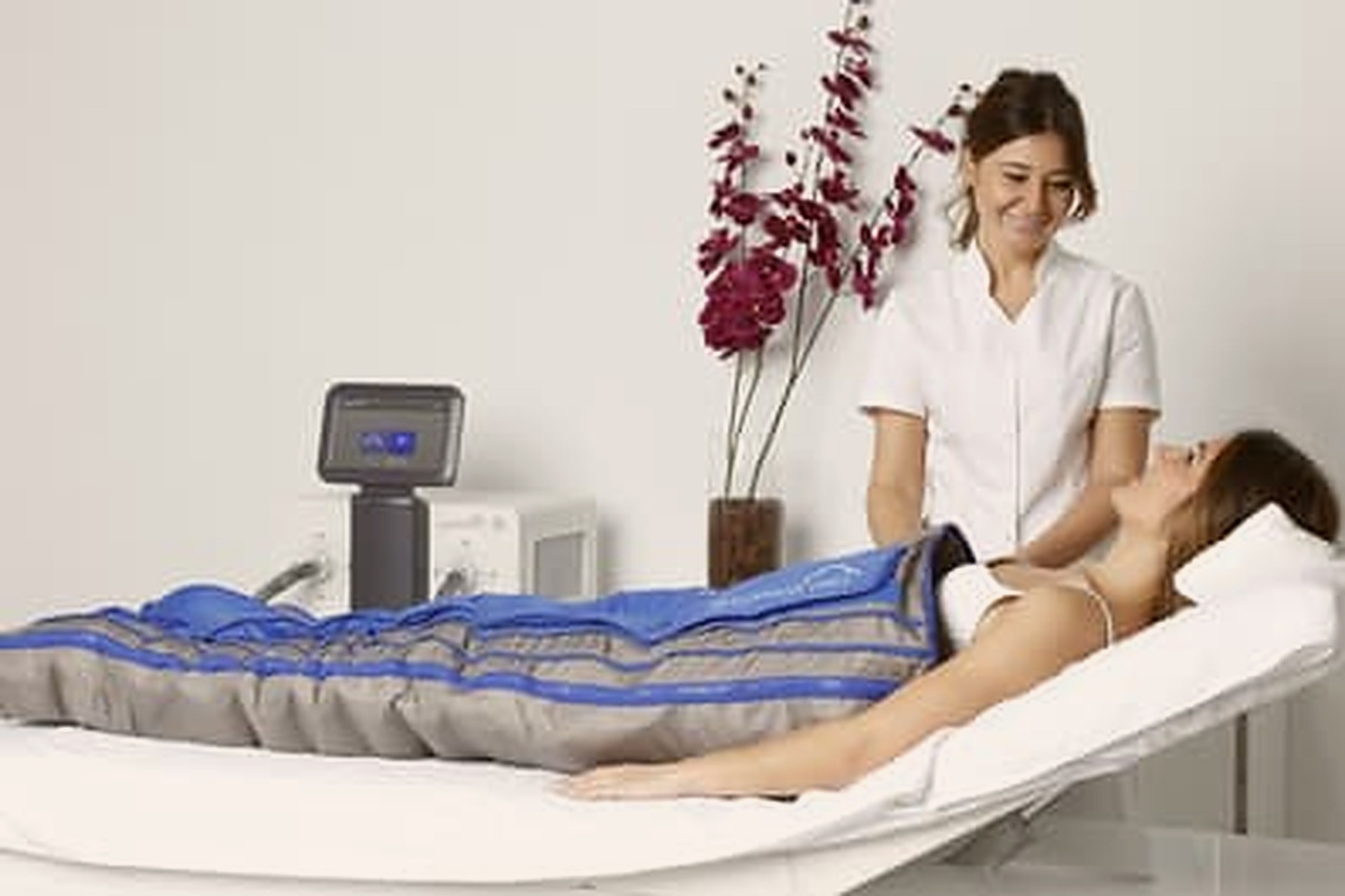 Kundin in einer Druckmanschette zur Lymphdrainage, Therapeutin steht daneben